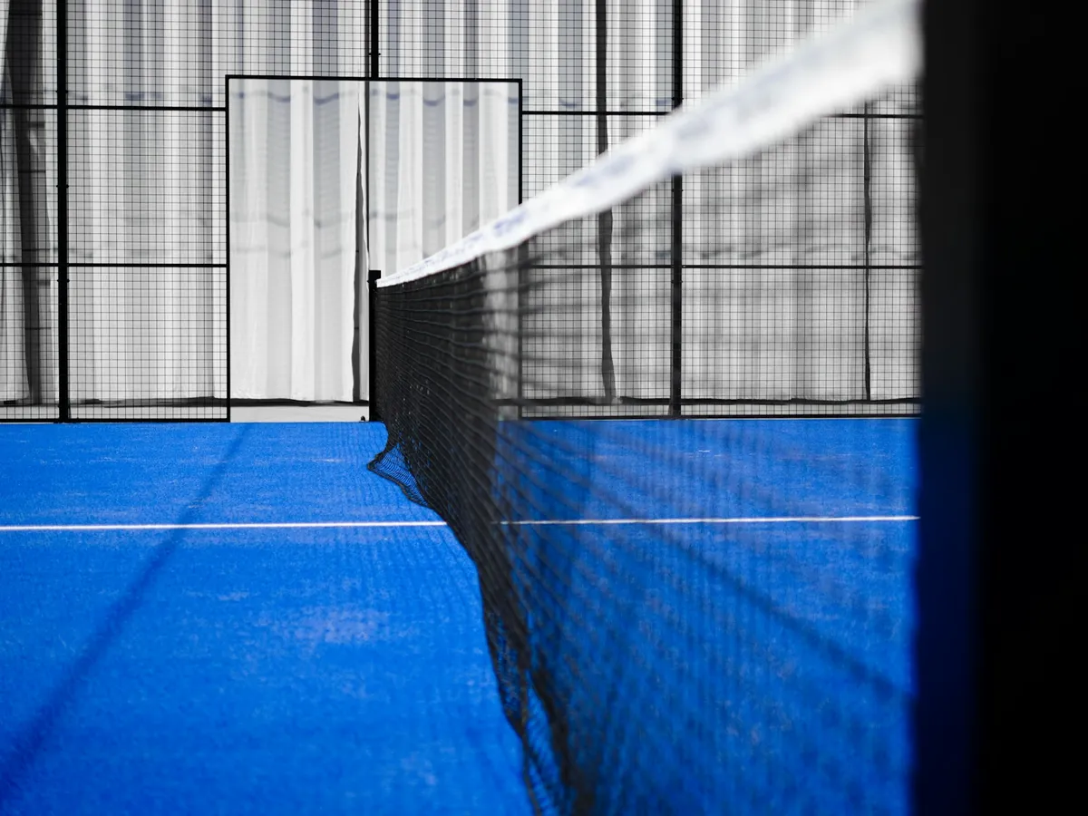 Le filet d’un terrain de padel couvert, vu dans sa longueur, sur un gazon bleu