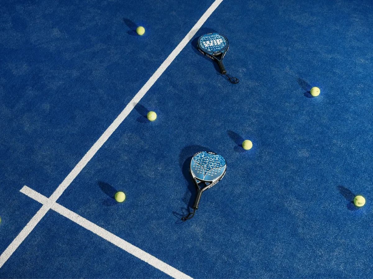 Deux raquettes de padel et des balles posées sur un terrain bleu, vues de haut