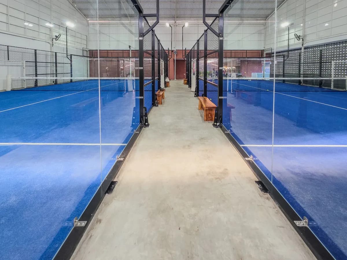 Allée entre deux terrains de padel couverts, avec leurs vitres
