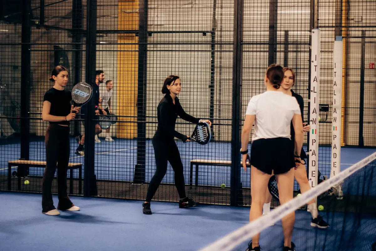 Quatre joueuses et joueurs sur un court de padel couvert, en plein échange.